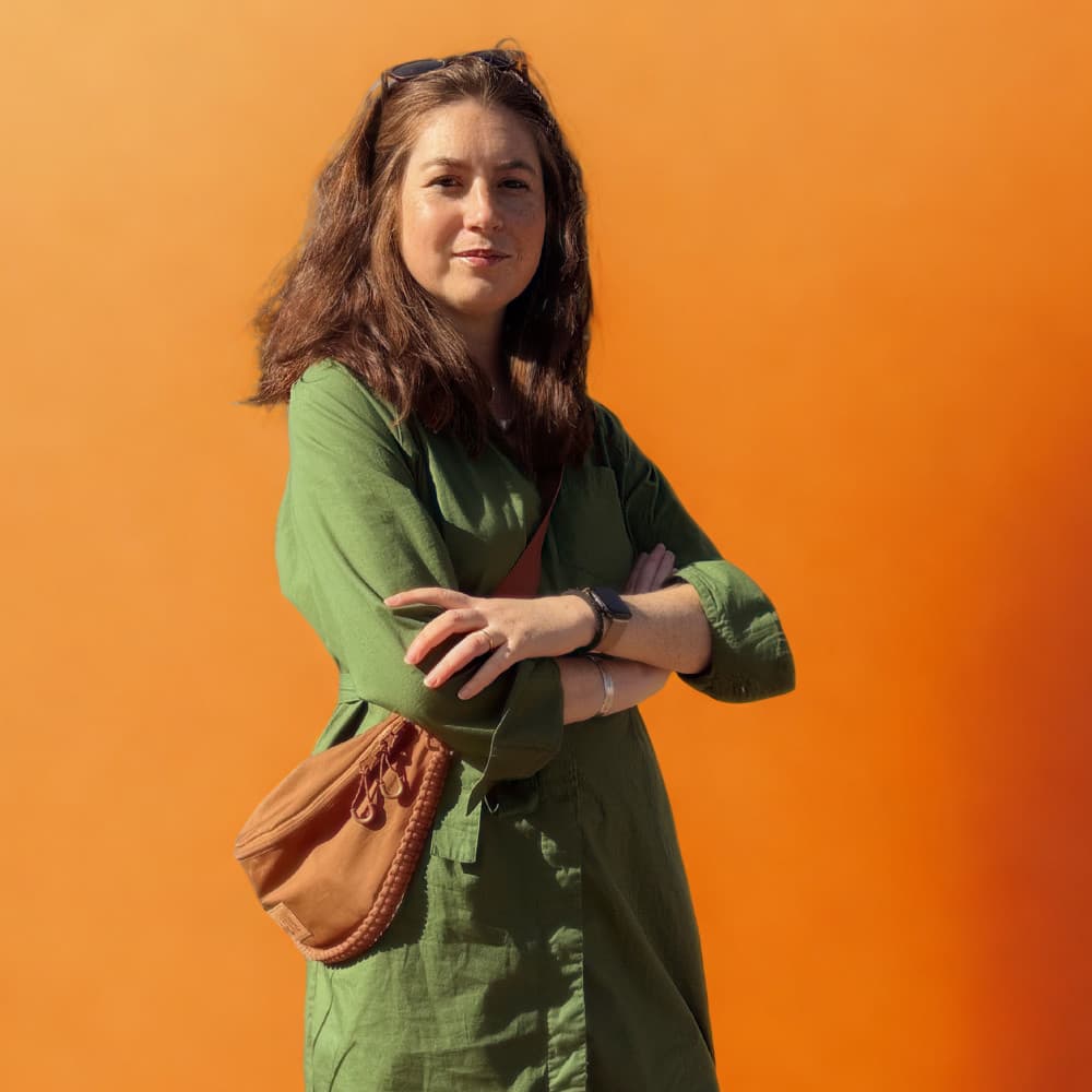 Elana Reinholtz with arms crossed against an orange backdrop